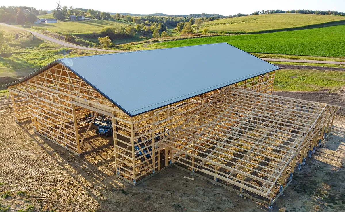 Aerial view of a post-frame farm building with a metal roof beside green fields