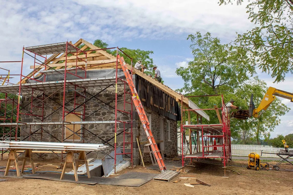 Crew working on an old stone house’s roof, with new framing, dark underlayment and scaffolding