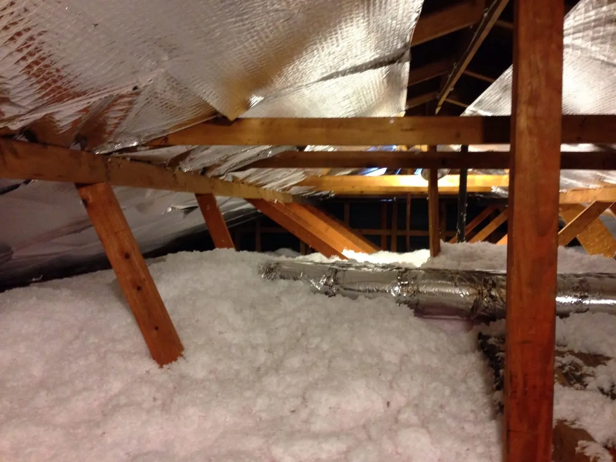Insulated flexible duct running across attic insulation under a foil radiant barrier