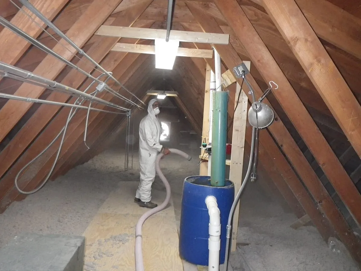 Attic with wooden rafters and roof boards, insulation being blown across the floor