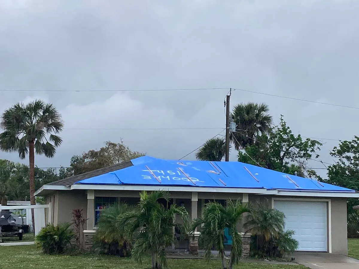 Single-story house with its whole roof covered in blue plastic sheeting