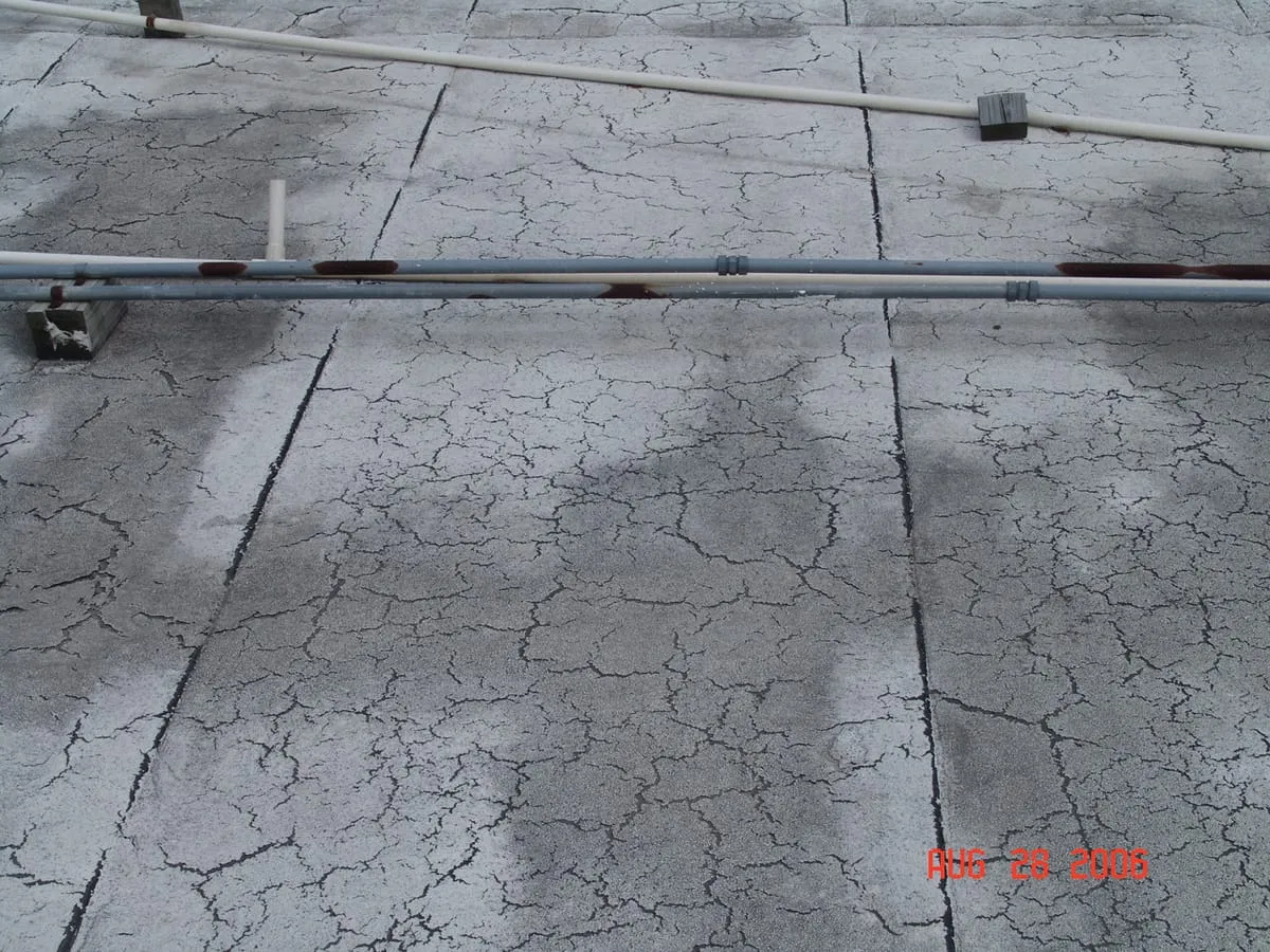 Flat roof coating cracked all over its surface, with pipes running across it