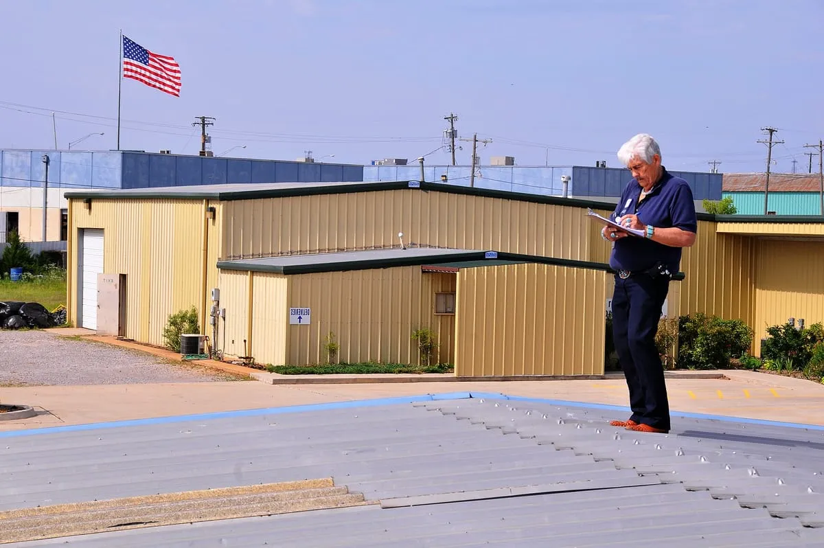Inspector with a clipboard documenting damage on a low-slope metal building roof