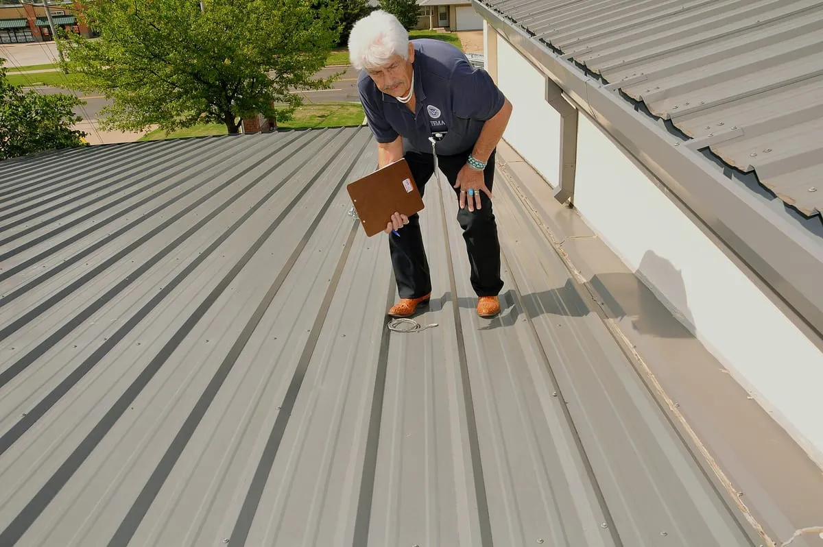 Inspector with a clipboard bending to look closely at a metal roof surface