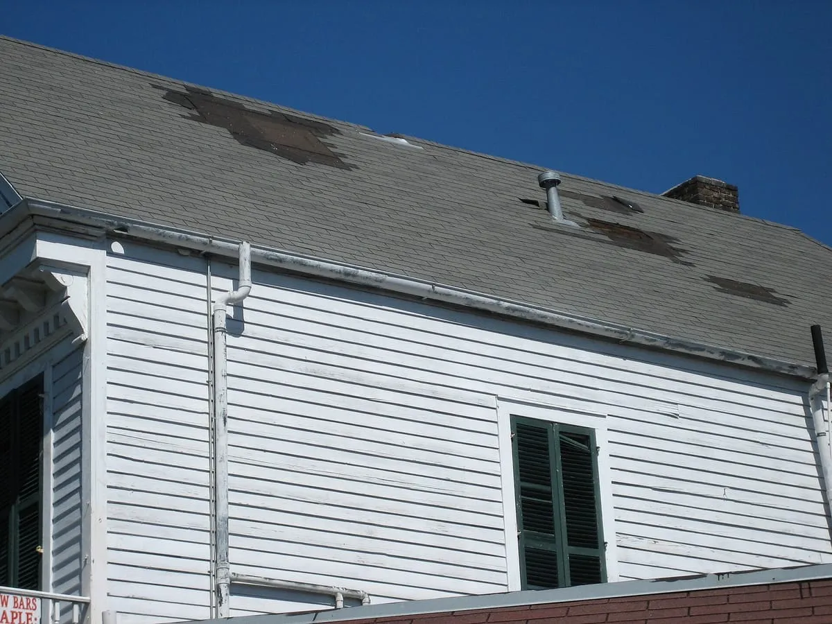 Shingle roof with several patches of missing shingles, seen from the ground