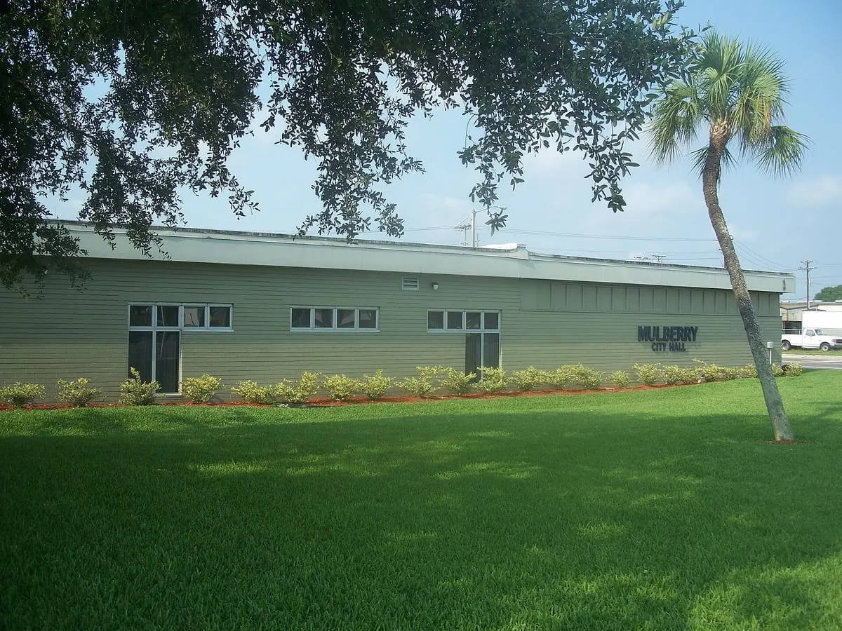 Single-story Mulberry City Hall building with green siding behind a wide lawn