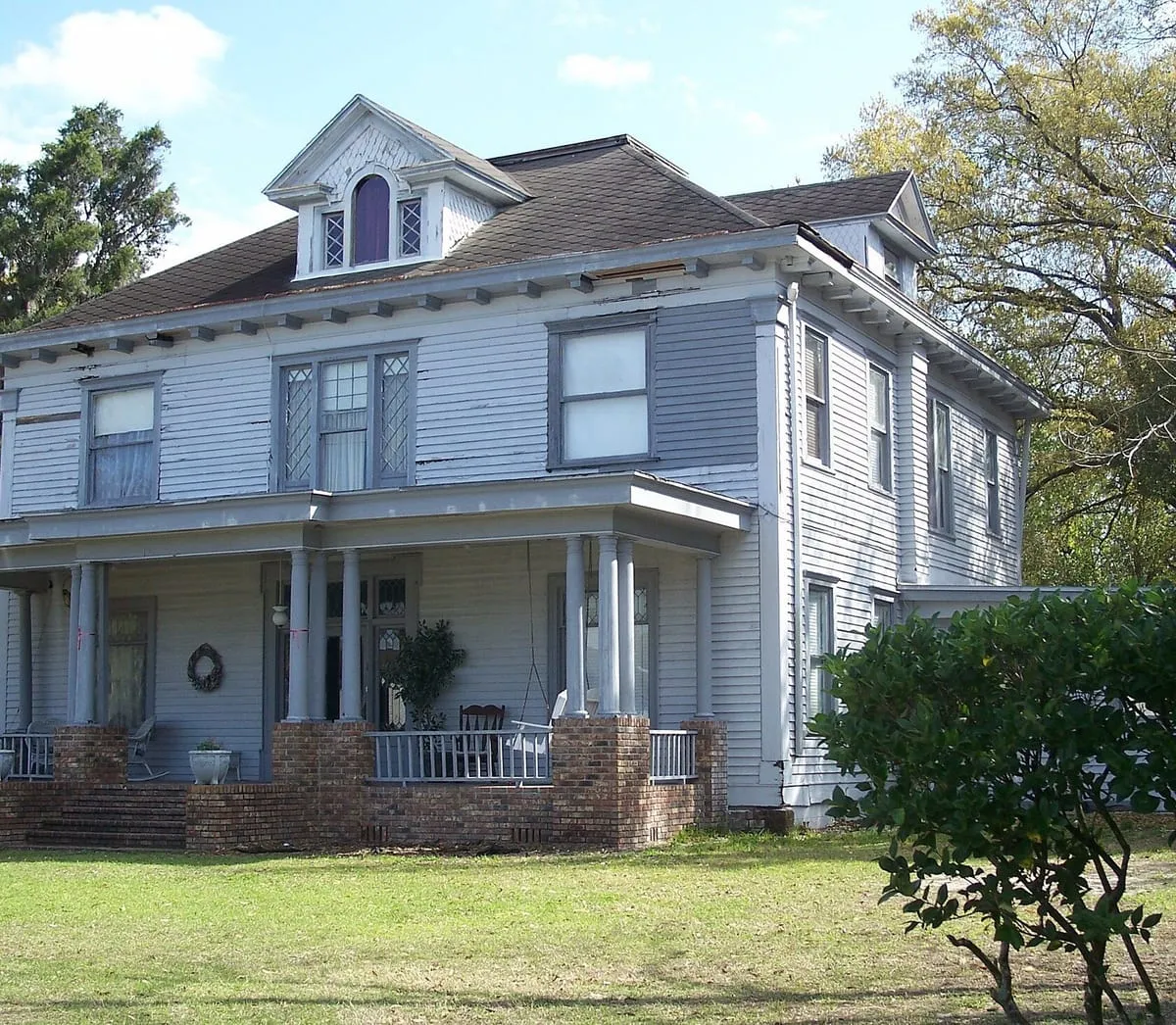 Two-story frame house with a hipped shingle roof, dormer and wide porch in Plant City