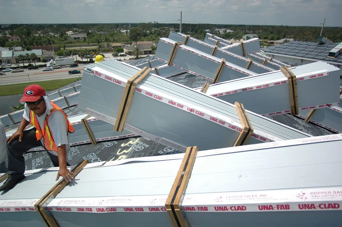 Worker sitting among bundled metal roof panels laid across a roof covered in underlayment