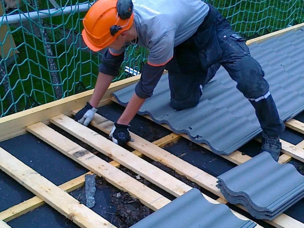 Roofer in a hard hat laying gray roof tiles onto wooden battens