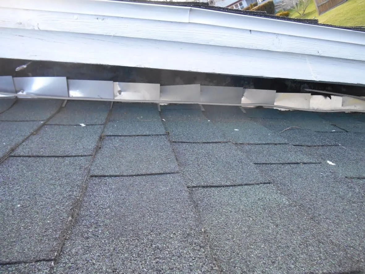 Step flashing along a wall left exposed and gapped above asphalt shingles
