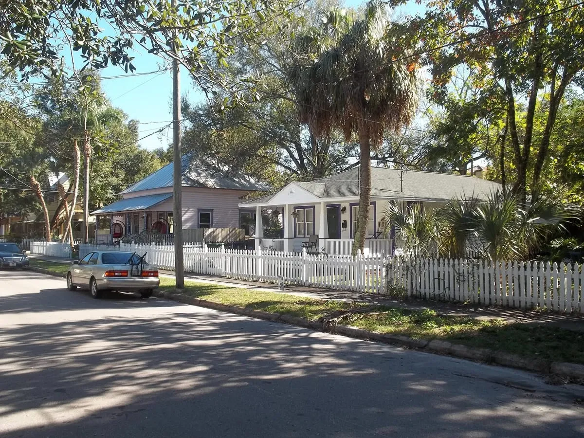 Frame cottages with metal and shingle roofs behind a white picket fence in Tampa Heights