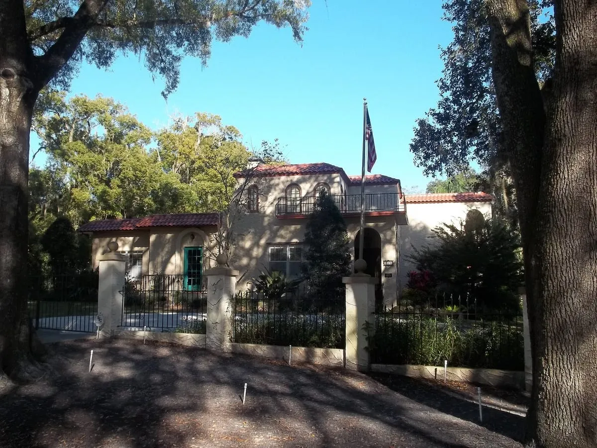 Mediterranean Revival house with a red clay tile roof behind a gated wall in Temple Terrace