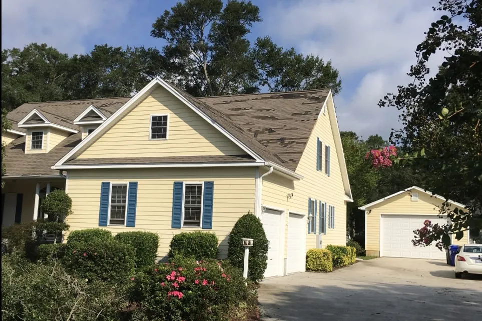 Two-story house with patches of shingles torn off one side of its roof