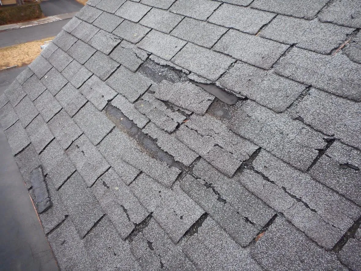 Worn asphalt shingles with cracked, torn and missing pieces across a roof slope